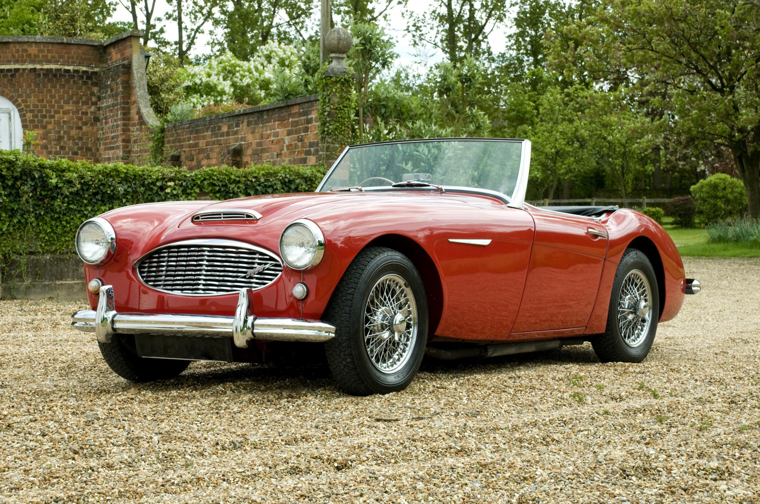 A classic red sports car parked on gravel drive seen from the side