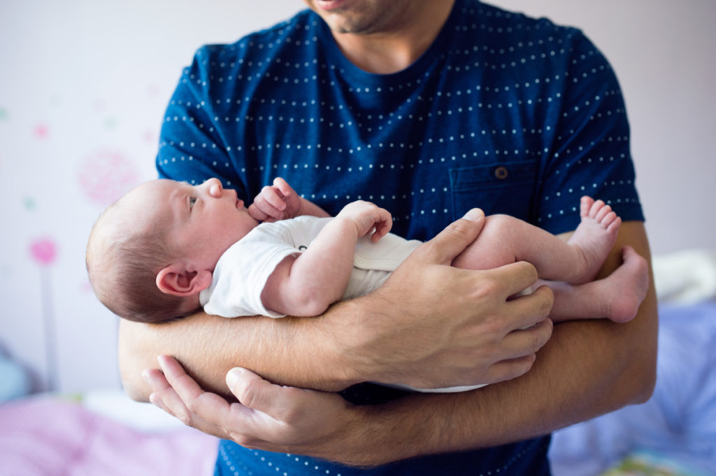 Close up of young father holding his newborn baby son in his arms