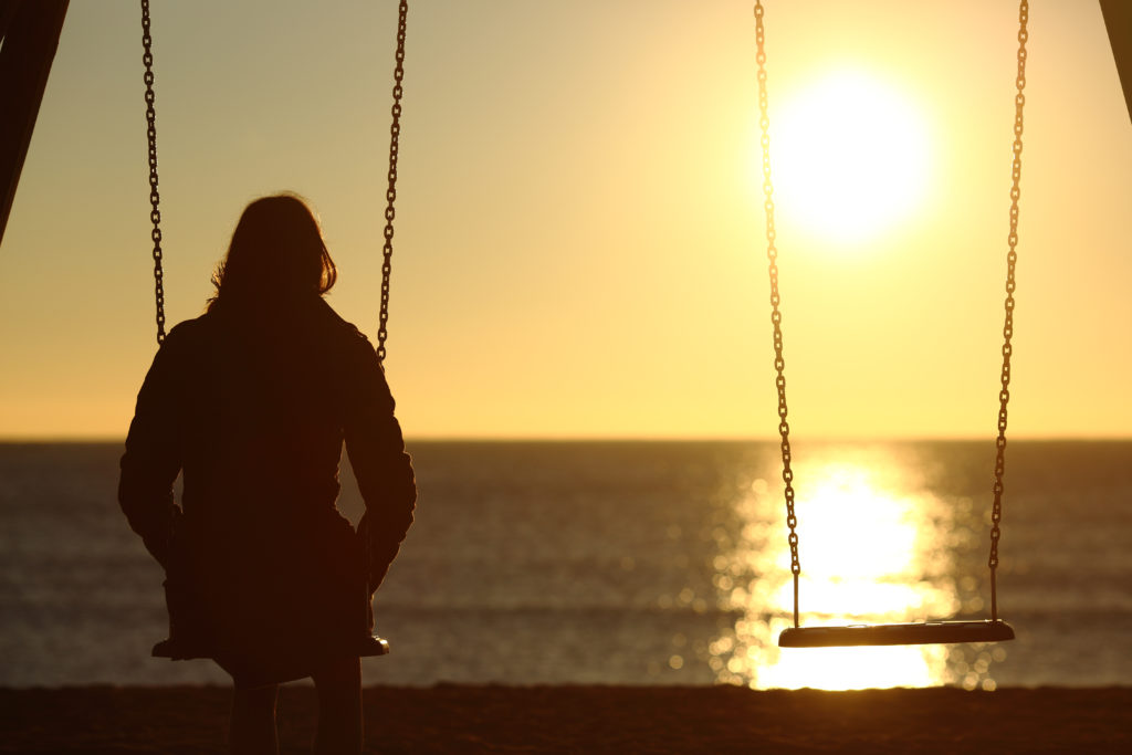 Lonely woman watching sunset alone in winter on the beach at sunset