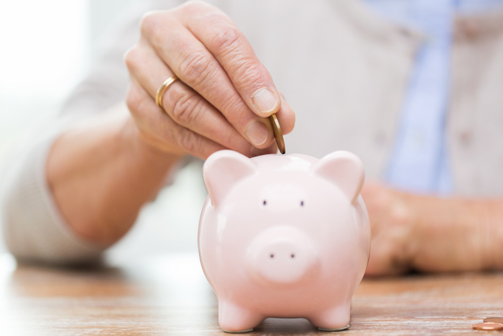 future inheritance after divorce uk concept - elderly lady putting coins into a pink ceramic piggy bank