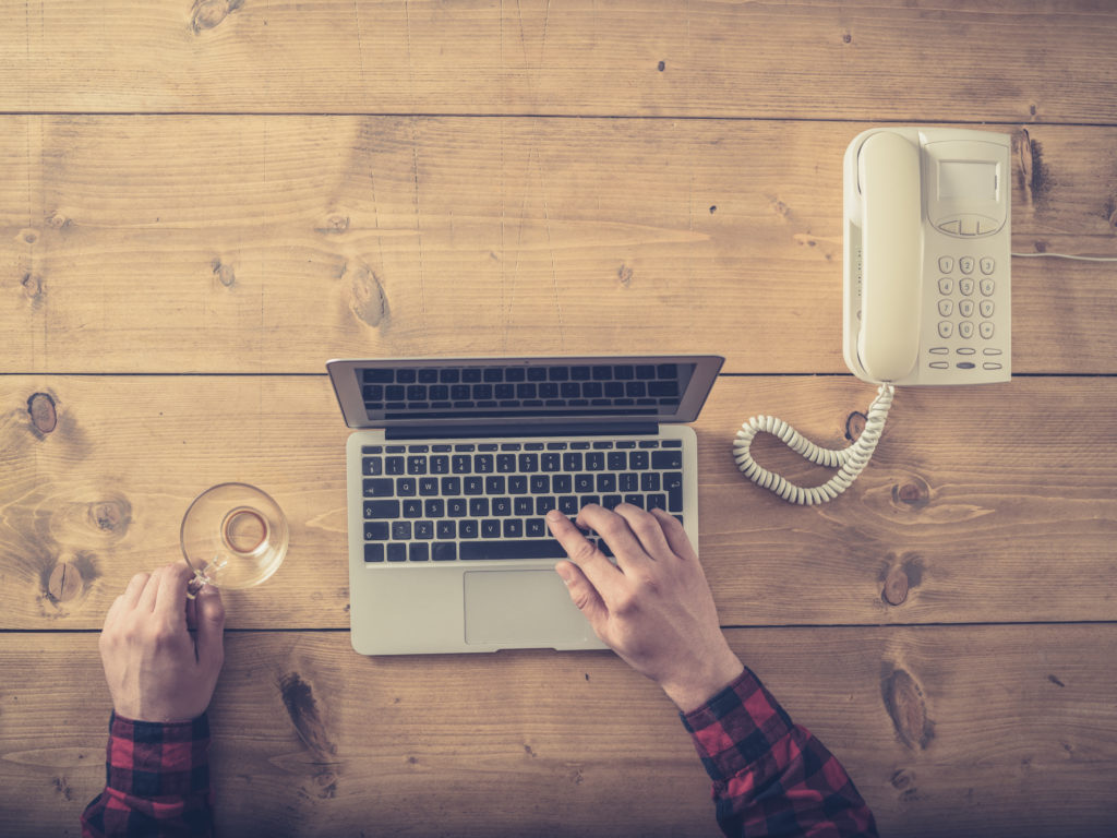 Overhead shot of a man using a laptop and an old wired telephone