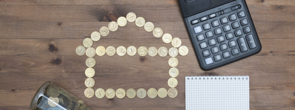 coins in house shaped, calculator pen and notebook on old wooden table