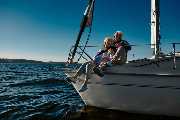 retired couple sitting in the sun on their yacht, happy after buying a boat