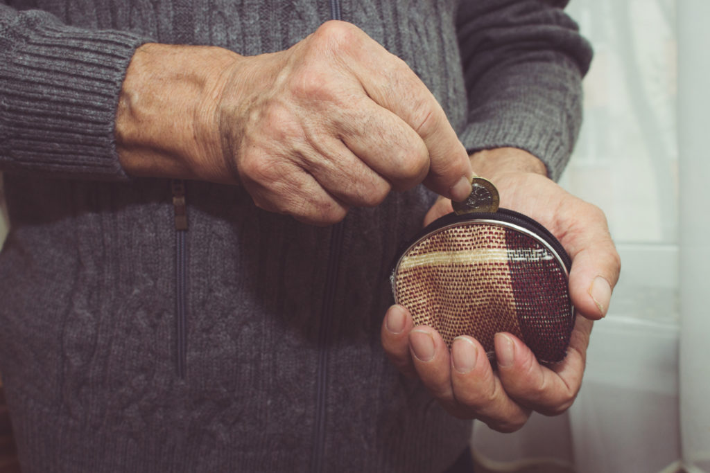 An elderly man puts a coin in an empty wallet. Poverty in retirement concept.