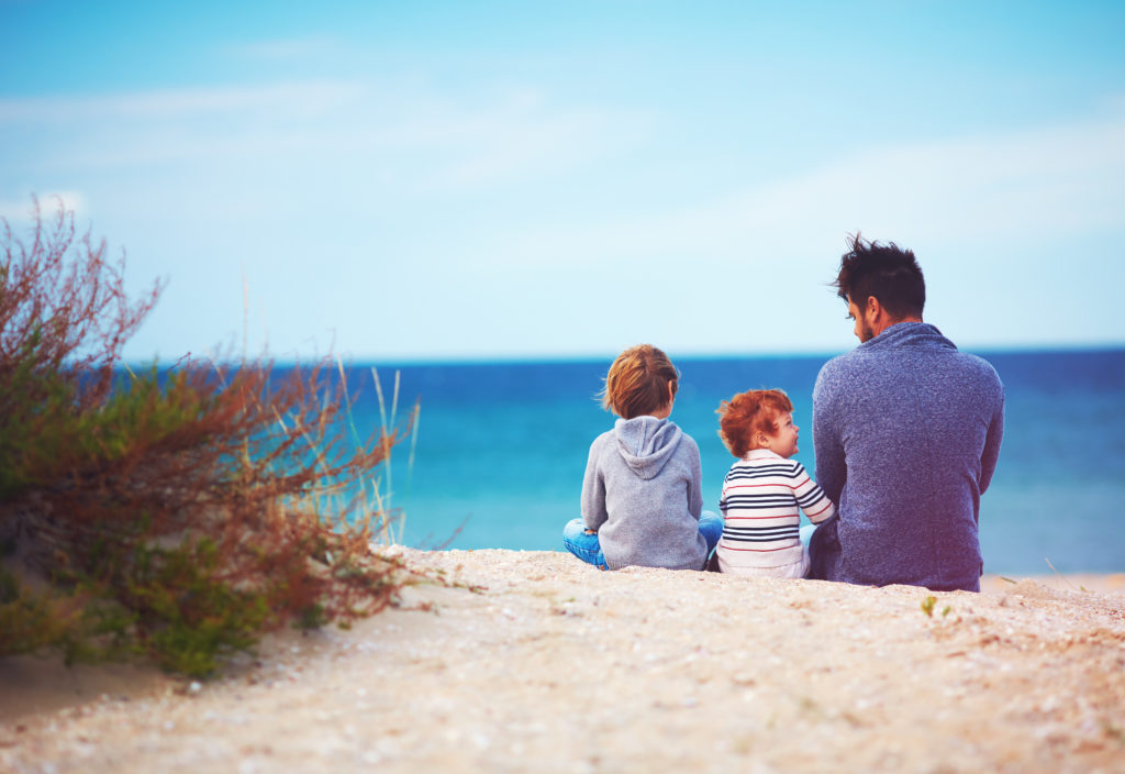 father and sons at sandy beach near the sea on windy day