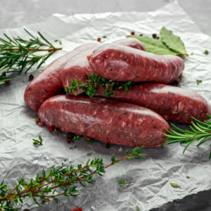 Freshly made raw breed butchers sausages in skins with herbs on crumpled paper