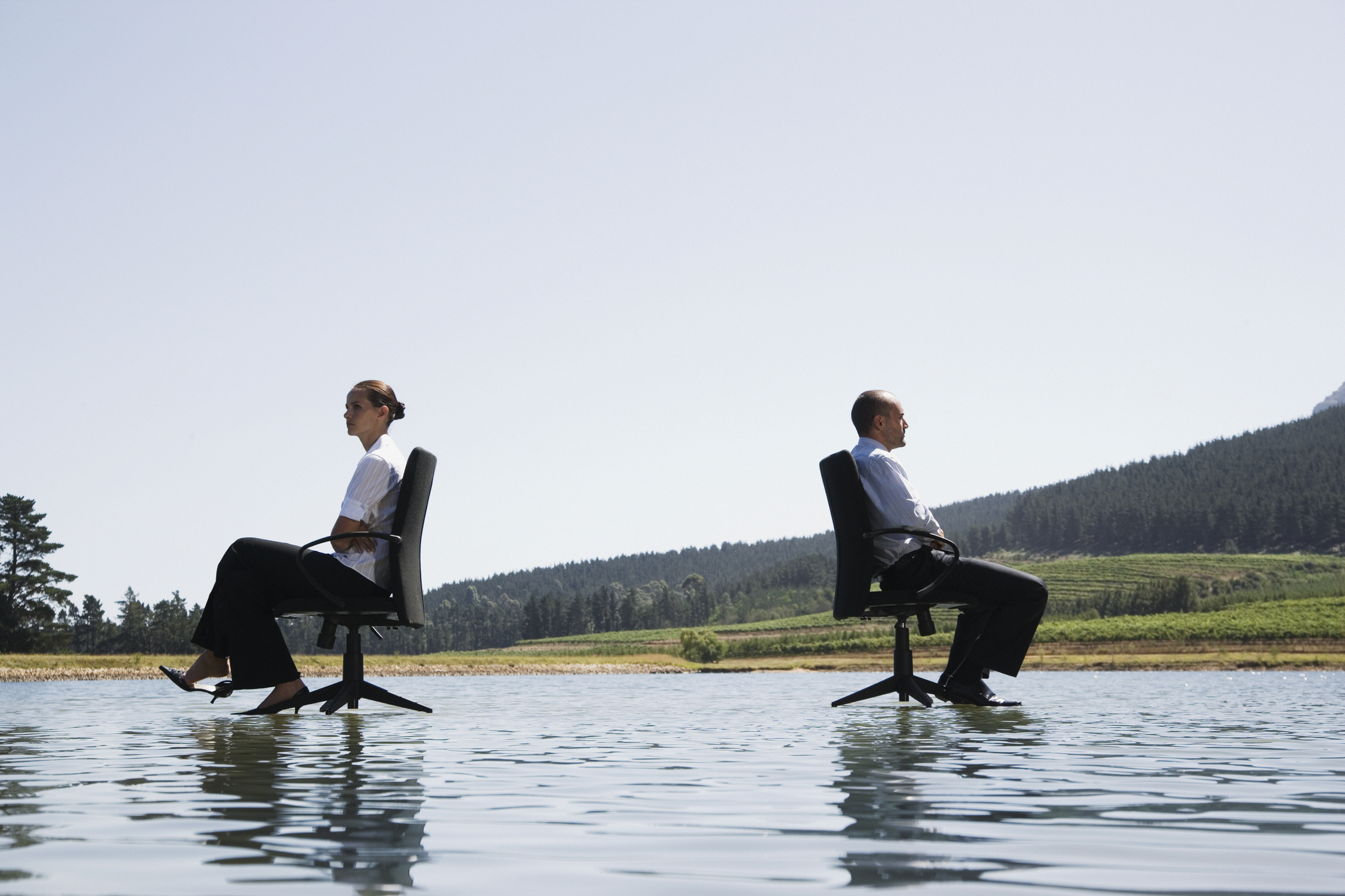 Businessman and woman in office chairs on water facing away