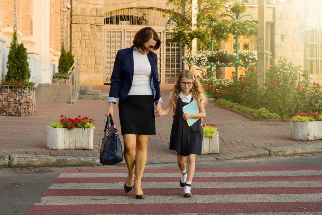 A woman and young schoolgirl holding hands, on zebra crossing