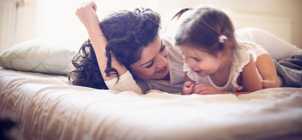 Happy young single mother playing with her little girl on the bed