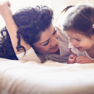 Happy young single mother playing with her little girl on the bed