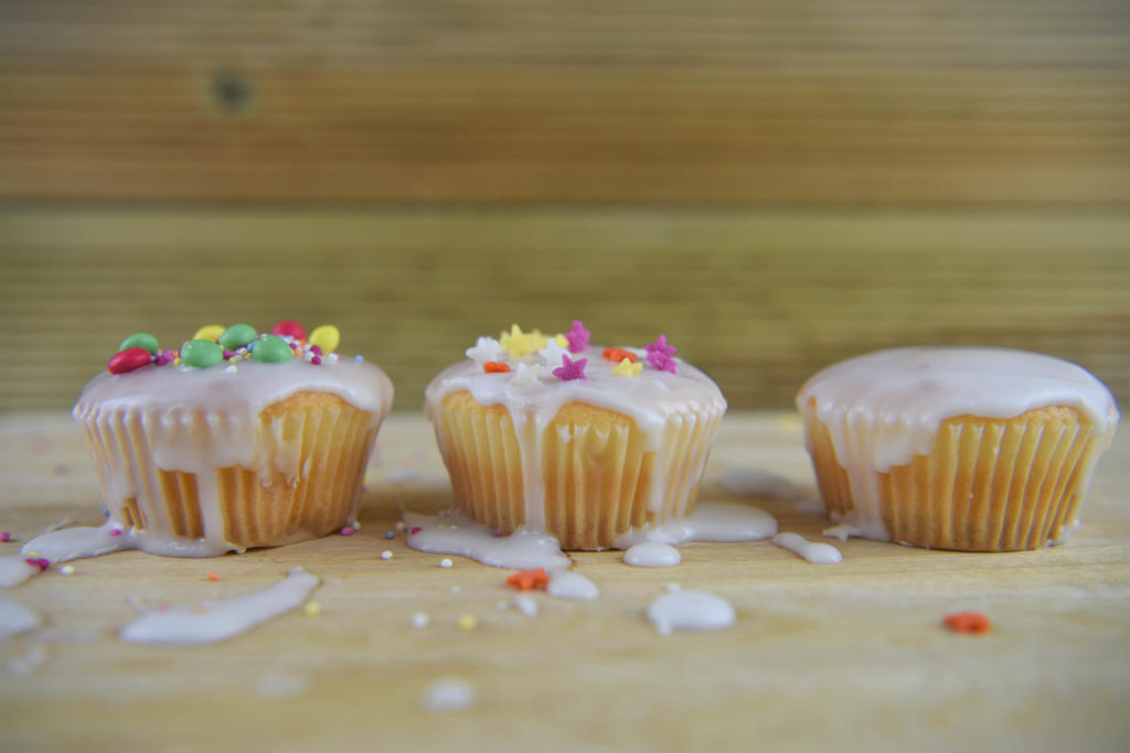 mini cakes being decorated with icing on a messy kitchen table