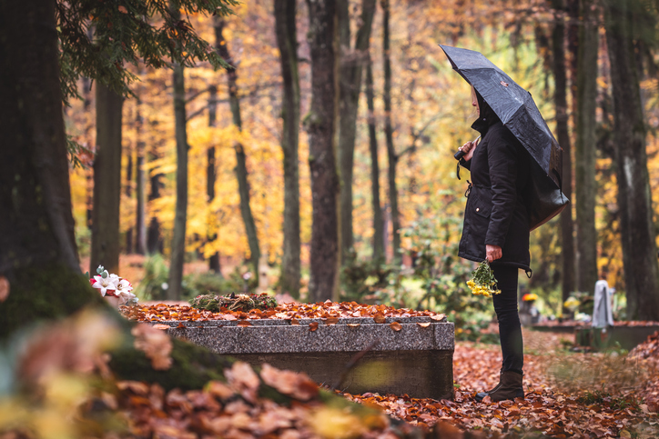 Woman standing over a grave under a black umbrella, mourning. Autumn scene