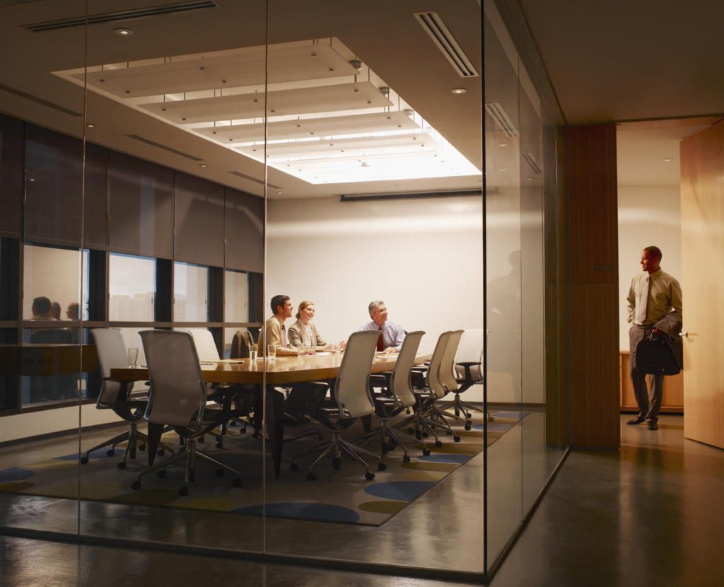 Three businesspeople in boardroom watching businessman leave