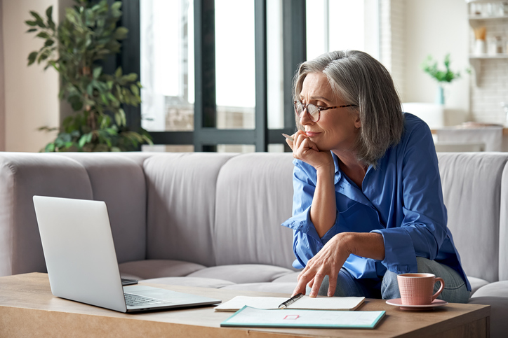 Businesswoman reviewing paperwork and computer screen while sat on a sofa