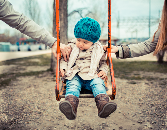 A child on a swing with one arm from each parent helping the child swing.