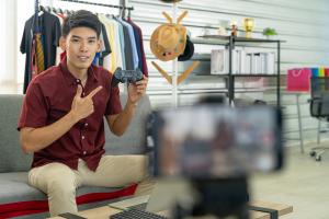 brand influencer holding up computer game controller in front of video captured on smart phone for marketing purposes