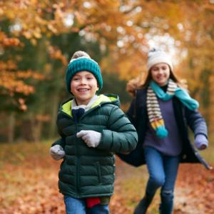 two children run through fallen autumn leaves in woodland