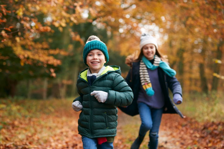 two children run through fallen autumn leaves in woodland