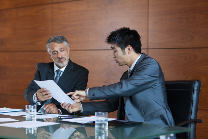 Two business people sitting down to discuss employers business sale review paperwork