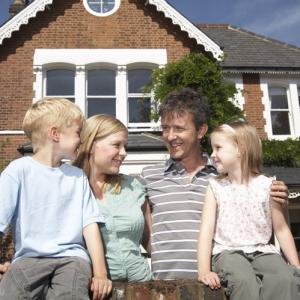 couple outside red brick family home with their two children