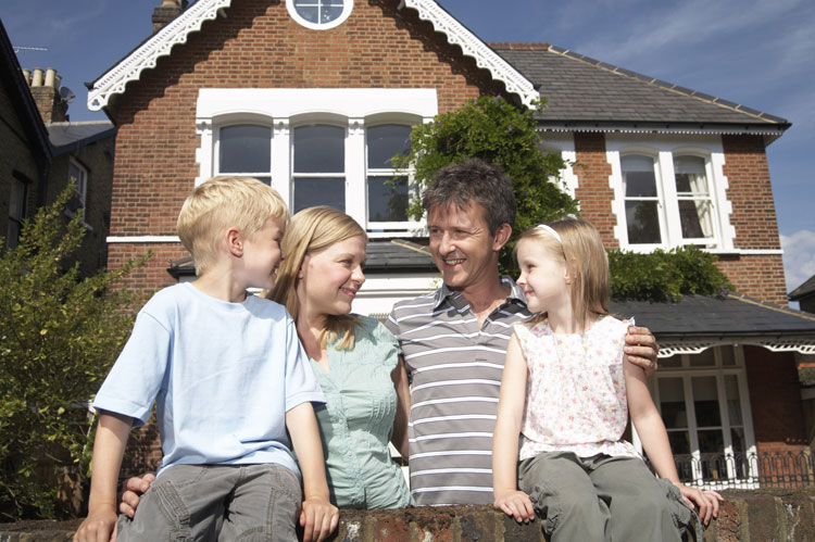 couple outside red brick family home with their two children