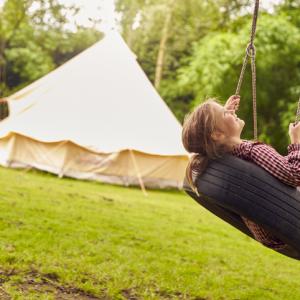 A child on a tyre swing in front of a yurt in a field, holiday accommodation