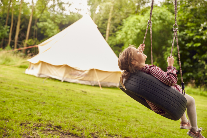 A child on a tyre swing in front of a yurt in a field, holiday accommodation