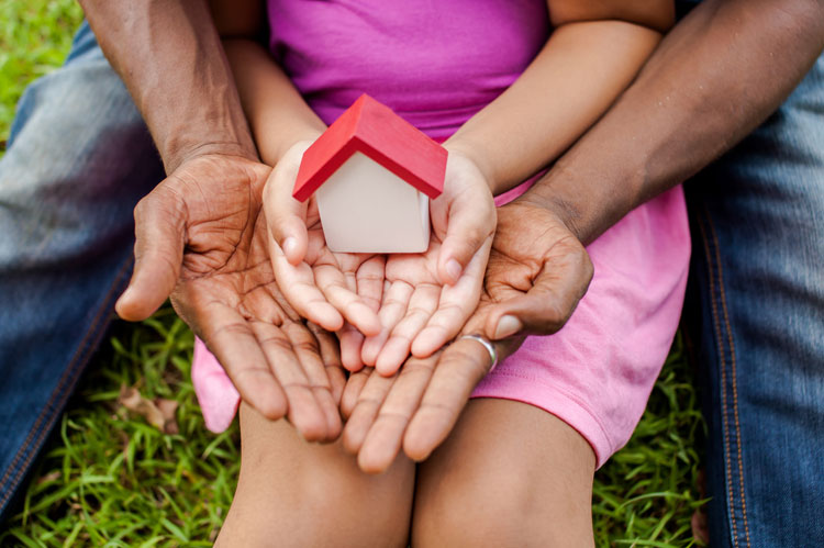 childs hands inside adults hands holding wooden house representing financial claim towards a child
