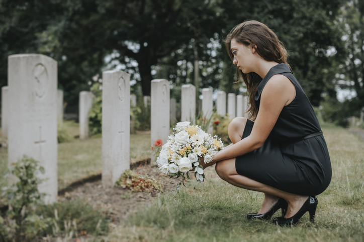 Woman in black laying flowers on a grave