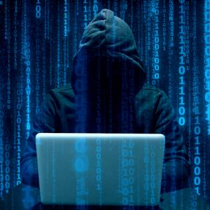 hooded figure on a laptop with 0s and 1s superimposed in blue lines. cybercrime concept.