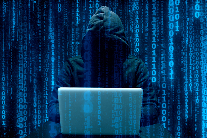hooded figure on a laptop with 0s and 1s superimposed in blue lines. cybercrime concept.