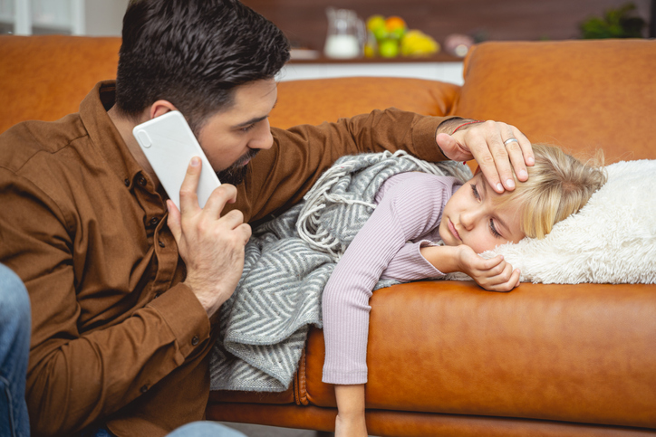 caring single dad with child who is ill on a contact weekend, touching her forehead for fever while on the phone