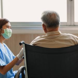 young woman, care home worker, helping an elderly man in a wheelchair