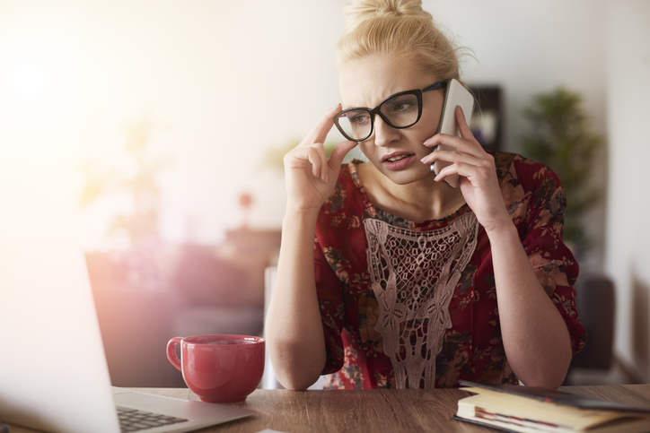 young blonde business woman in red top, on phone, looking at laptop with concern. concept for finding out she is personally liable for company wrongdoing