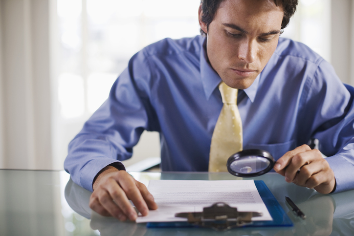 business man with a magnifying glass, reading the small print in a contract