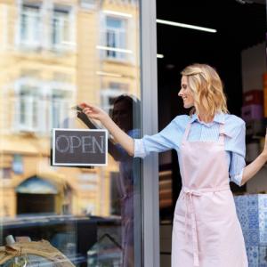 woman holding an open sign in front of a shop