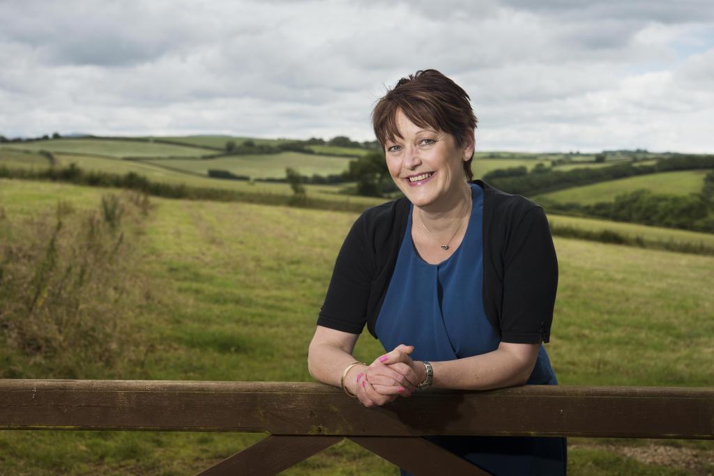 kate theophilus leaning against a farm gate with fields in the background