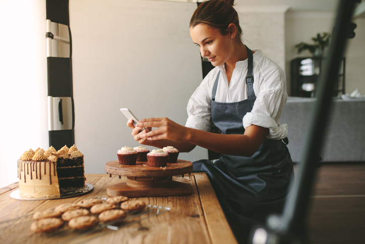 baker taking photograph of cakes on her phone for social media