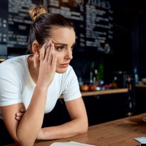 female owner of a leisure and hospitality business, leaning against coffee counter thinking pensively