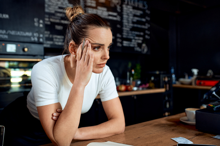 female owner of a leisure and hospitality business, leaning against coffee counter thinking pensively