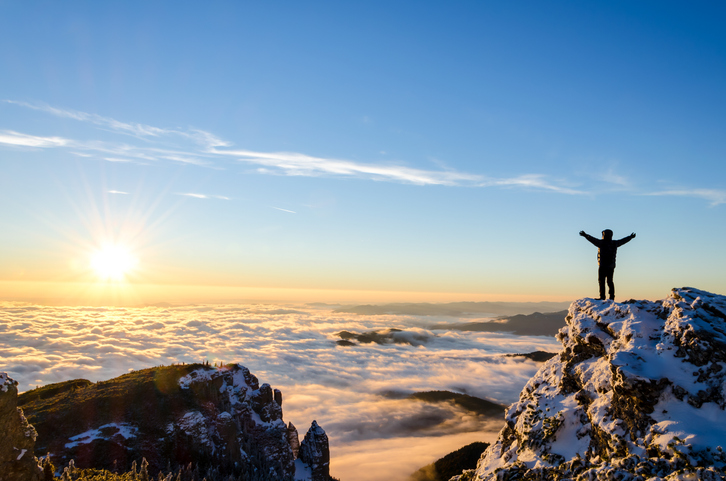 person silhouetted standing on the top of a mountain above the clouds, concept for new life after divorce