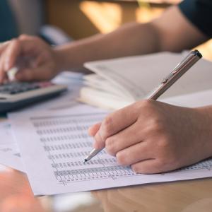 hands, one with pen working down a list of numbers, the other typing into a calculator. concept for commercial debts