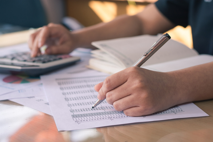 hands, one with pen working down a list of numbers, the other typing into a calculator. concept for commercial debts