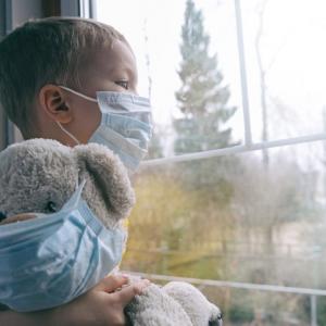 child looking out of window wearing mask, with teddybear wearing mask - concept for children in care
