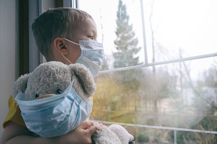 child looking out of window wearing mask, with teddybear wearing mask - concept for children in care