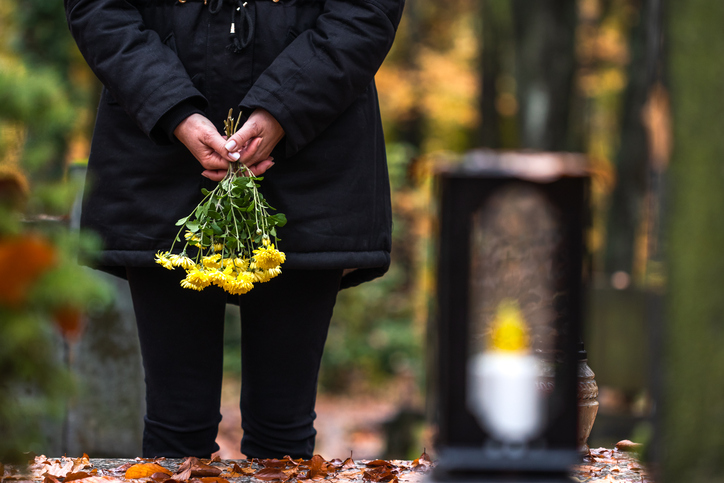 Woman holding flowers by a grave - concept for dealing with divorce after death