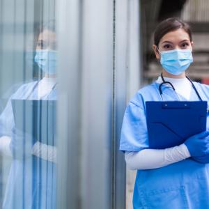 health care worker standing wearing mask and holding clipboard - concept for health care visa