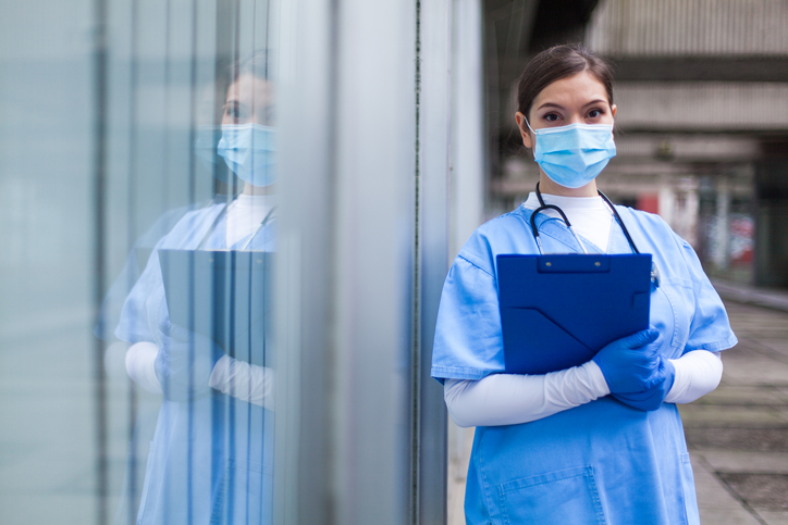health care worker standing wearing mask and holding clipboard - concept for health care visa