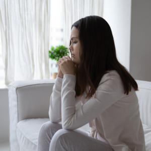 woman sitting alone on sofa, distressed by financial abuse