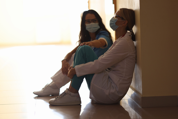 two women sitting on the floor, one comforting the other, both wearing masks. concept for invisible disabilities and mental health illnesses